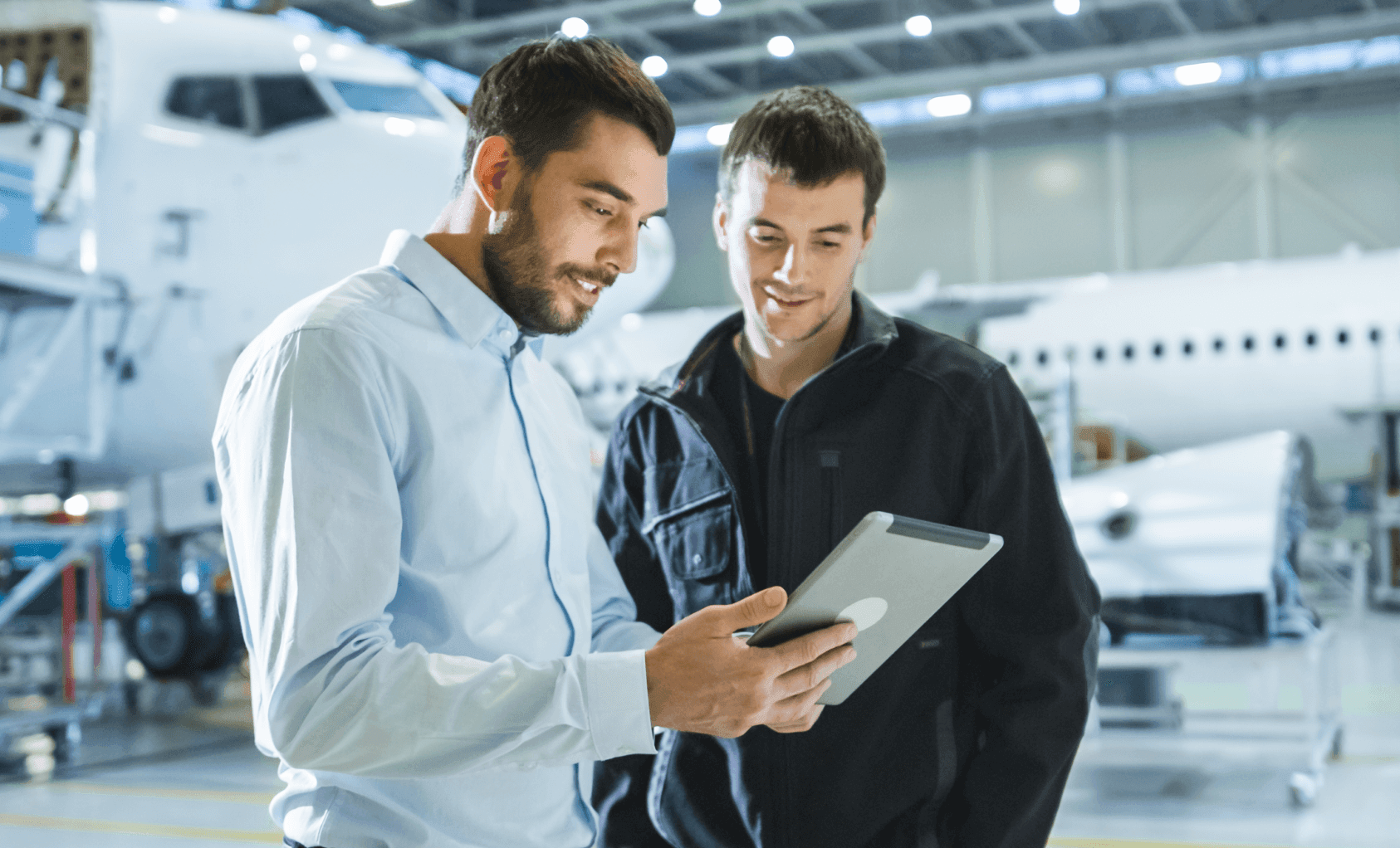Two men looking at an ipad with an aeroplane behind them