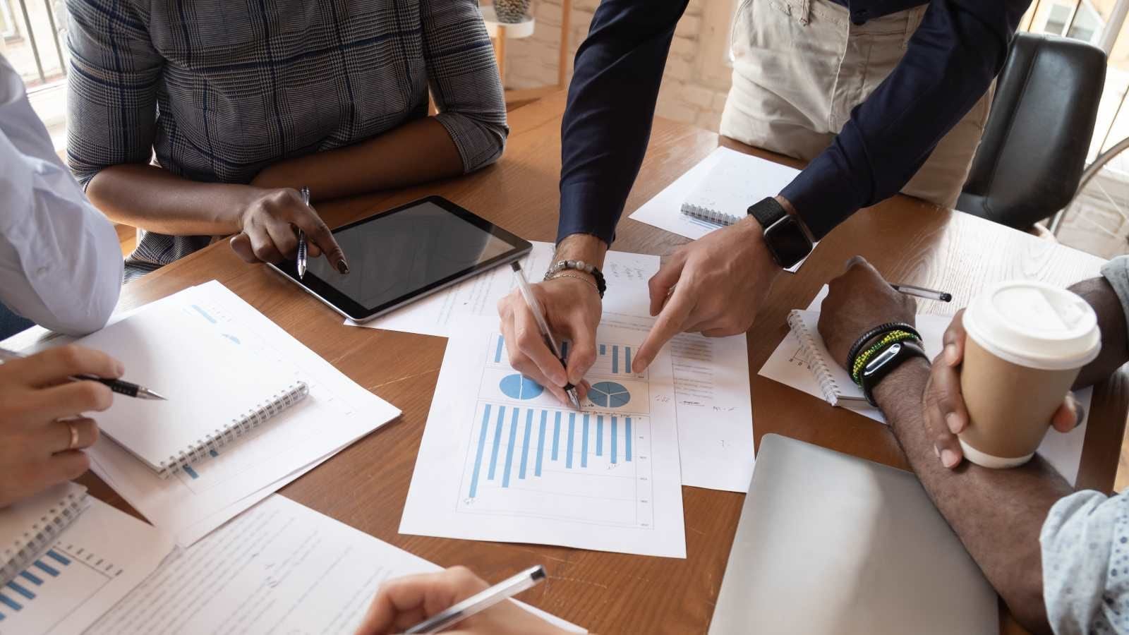hands on a table, some pointing at documents