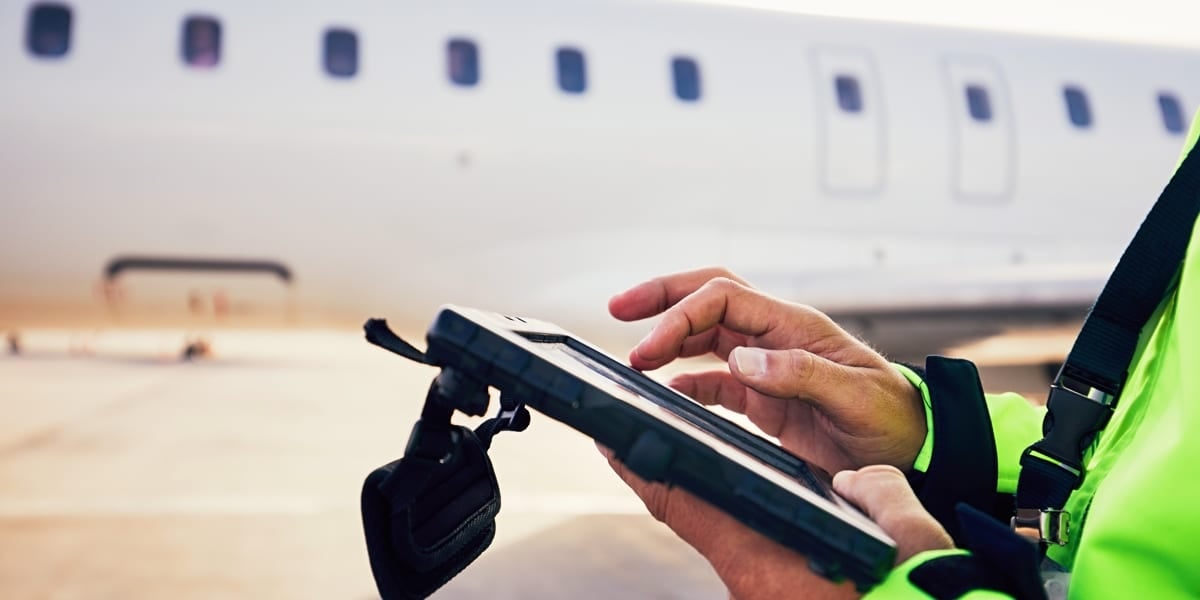 man in high vis looking at tablet next to aeroplane