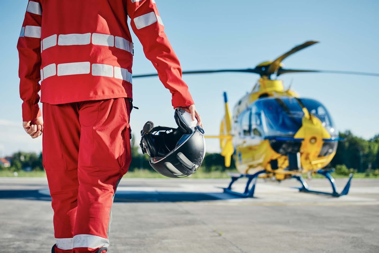 man with wearing high vis carrying helmet next to helicopter