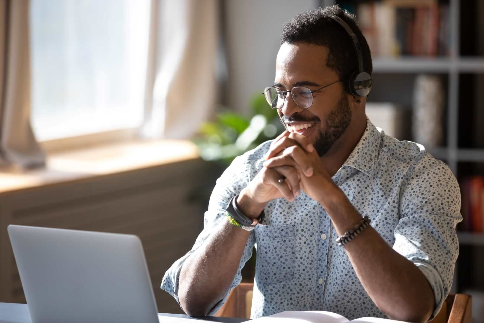 man in glasses smiling while looking at laptop